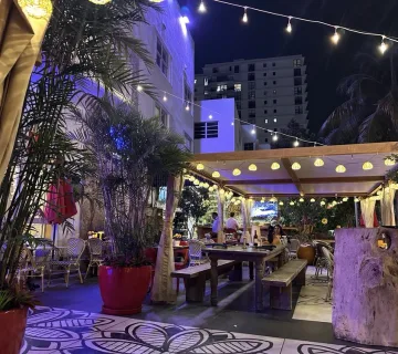 Outdoor patio with string lights, tropical plants, and dining tables at Maxine's Bistro & Bar in Miami Beach.
