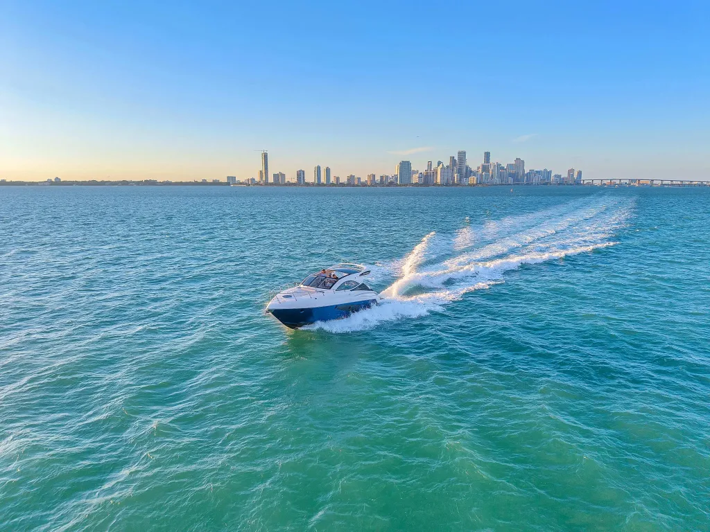 Speedboat gliding through clear blue Miami waters with city skyline in the background, bright sunny sky, and passengers enjoying the ride.