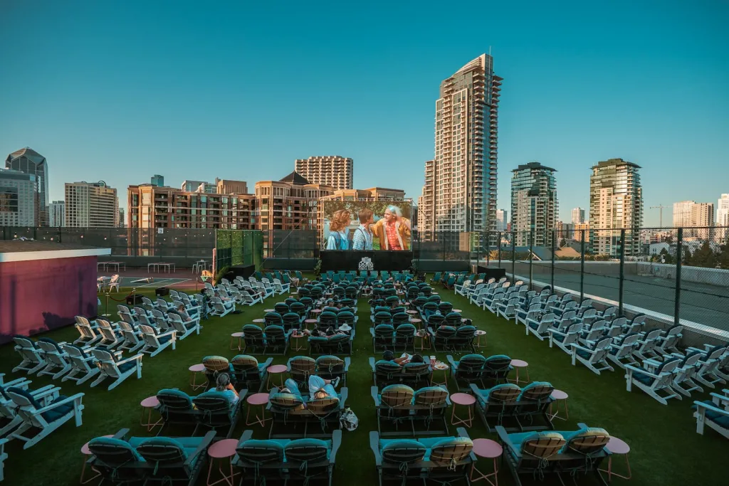 Couples enjoying Rooftop Cinema Club Miami under string lights with blankets, cocktails, and the movie playing overhead.