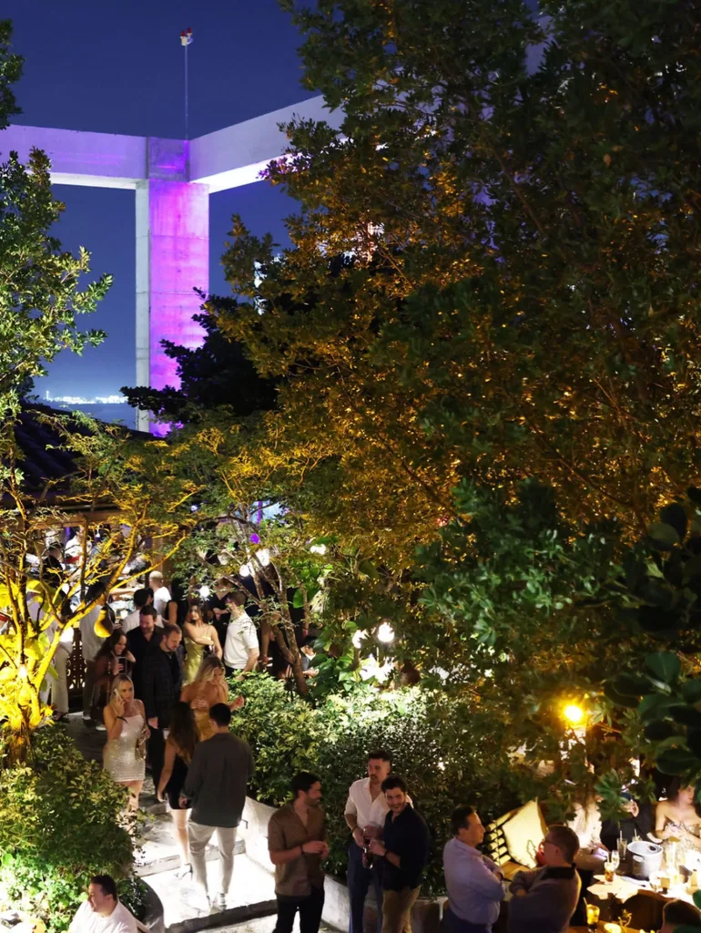 Sugar rooftop at night with glowing lights, Miami skyline backdrop, and a lively after-dark crowd