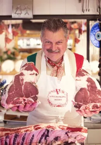 Italian butcher at Antica Macelleria Cecchini holding two large cuts of Bistecca Fiorentina in a traditional butcher shop setting.