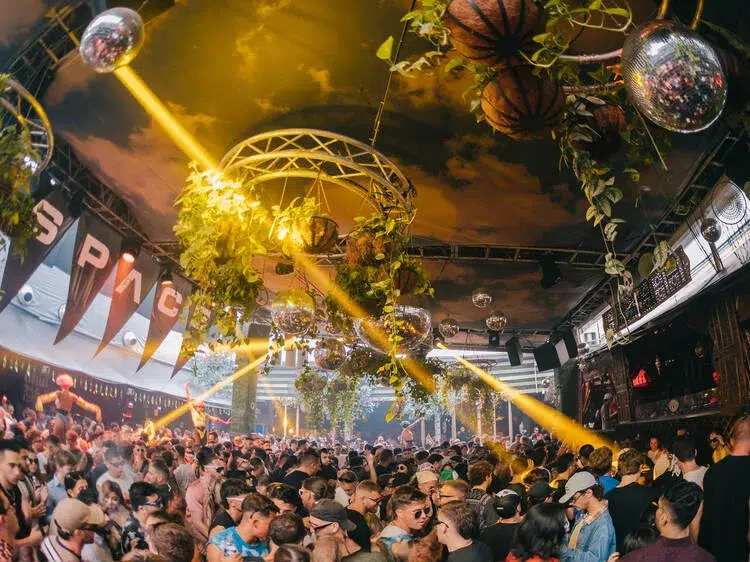 Nightclub in Miami with a packed dance floor, DJ booth lights, and a cheering crowd partying.