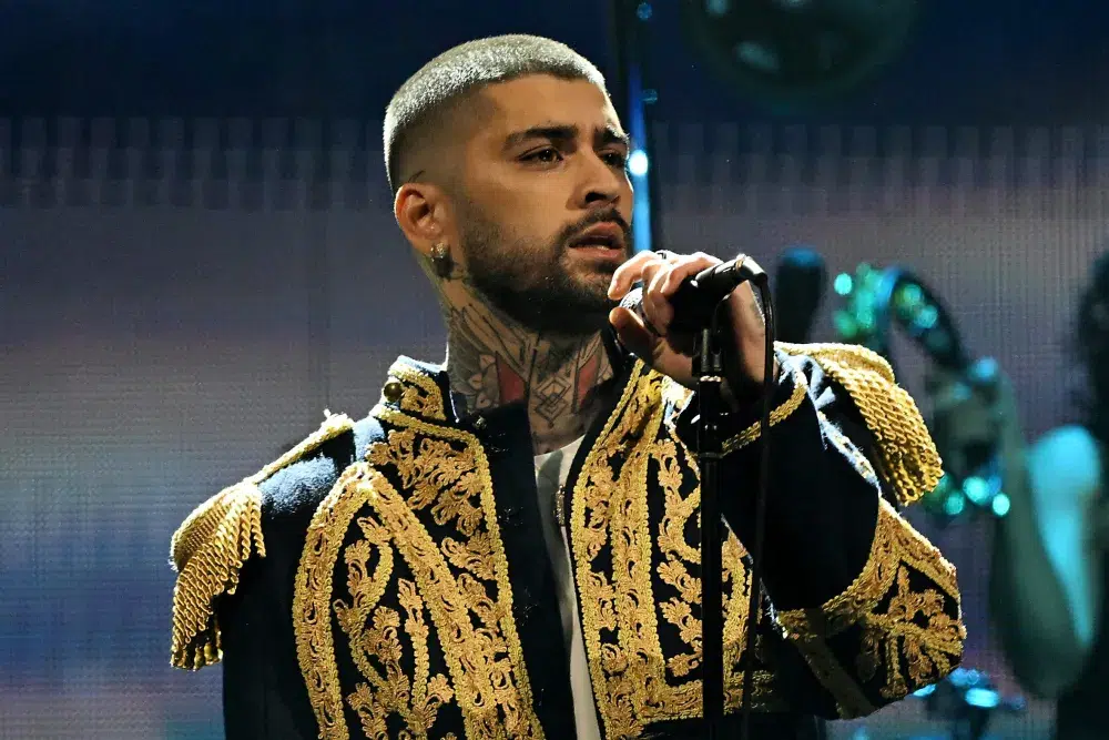 Zayn performing into a microphone at an arena show with the crowd cheering
