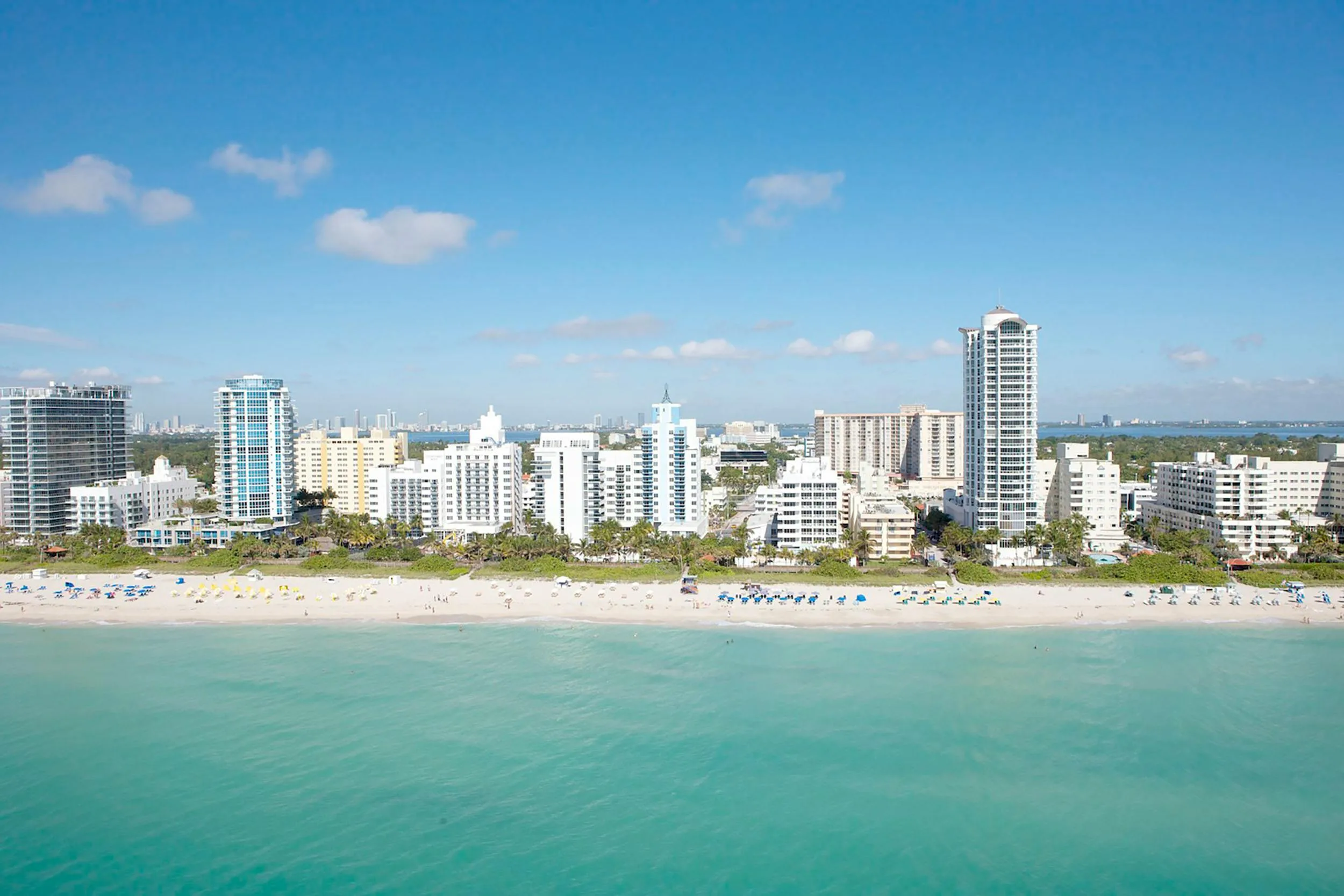miami beach Sunny view of Miami Beach with turquoise ocean water, soft sandy shore, gentle waves, and people relaxing along the coastline under a clear blue sky.