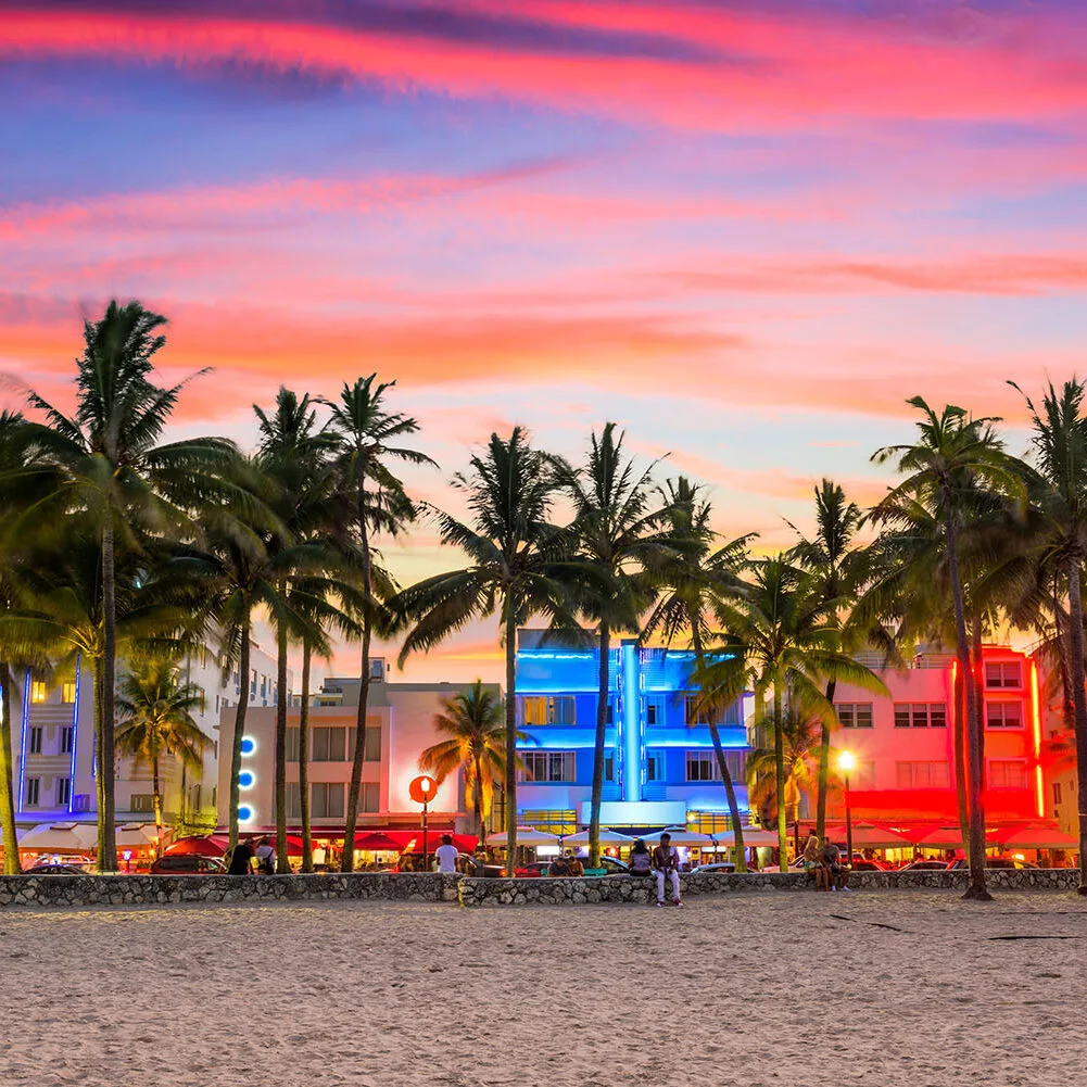 People relaxing by the ocean in Miami with colorful umbrellas and a clear blue horizon.