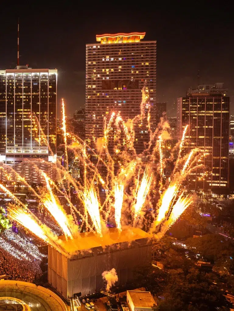 Fireworks exploding over the festival grounds while the crowd cheers under bright stage lights