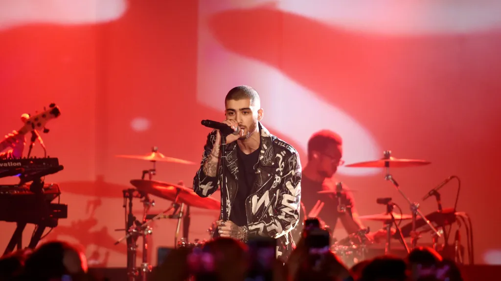 Zayn onstage under spotlights during a concert set with dramatic stage visuals