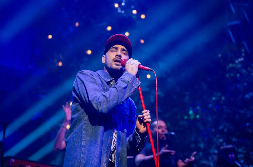 Zayn Malik singing on stage during a live concert with bright lights behind him