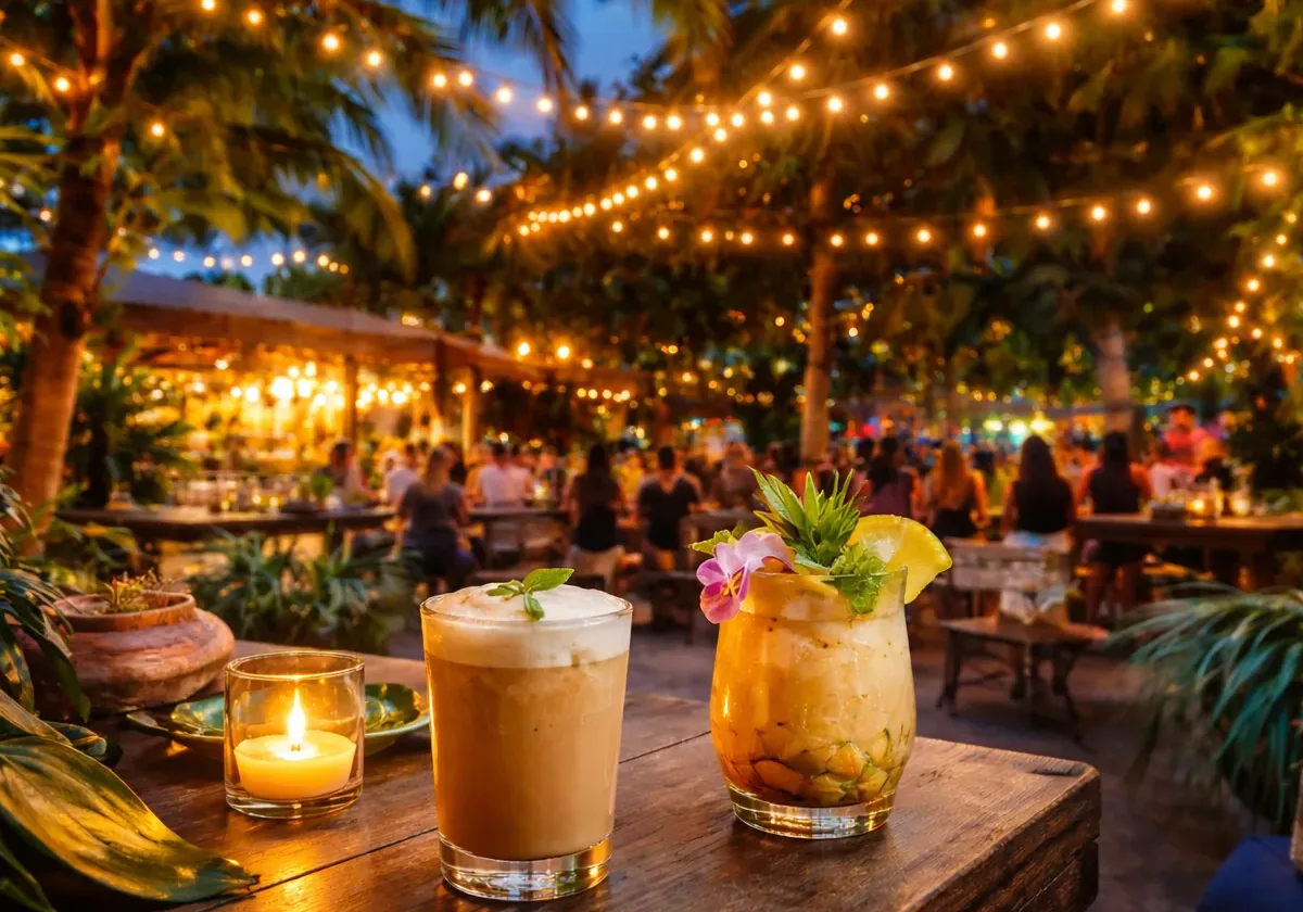 BestBarMiami Iced latte and tropical cocktail on a wooden table at a lush outdoor Miami Beach bar with palm trees and warm string lights at sunset.