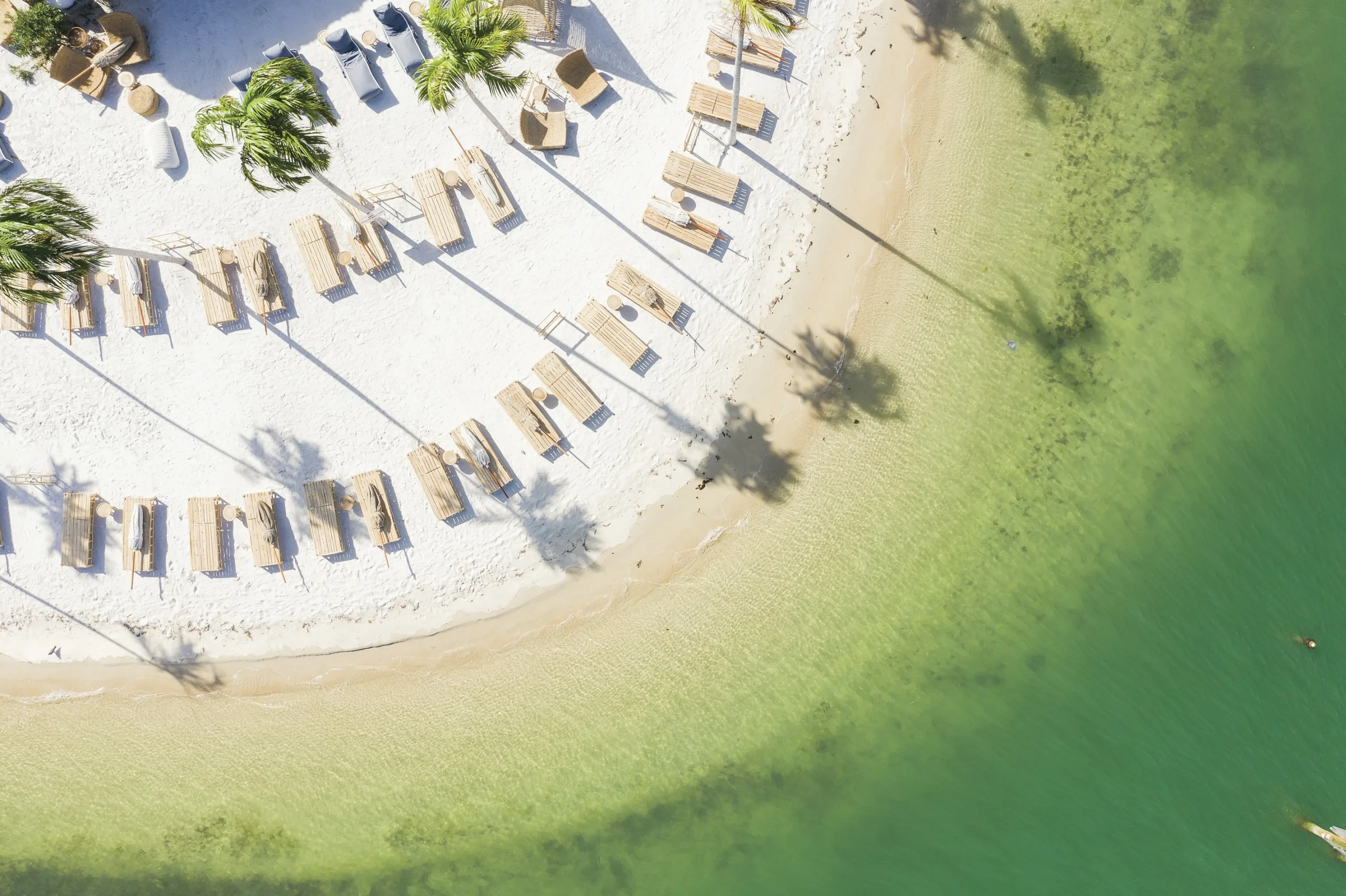 Aerial view of Joia with wooden loungers, white sand, and turquoise water