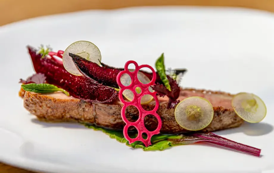 Gourmet steak dish with artistic beet garnish, radish slices, and microgreens on a white plate at a fine dining restaurant in Miami Beach.