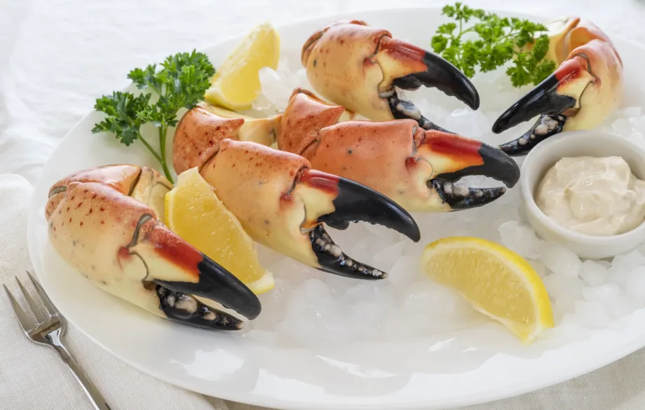 Fresh stone crab claws served on crushed ice with lemon wedges on a white plate at a Miami Beach seafood restaurant.