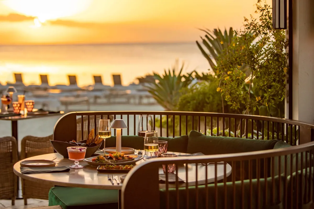 Sunset beachfront dining table with wine glasses and plates on a cozy outdoor terrace.