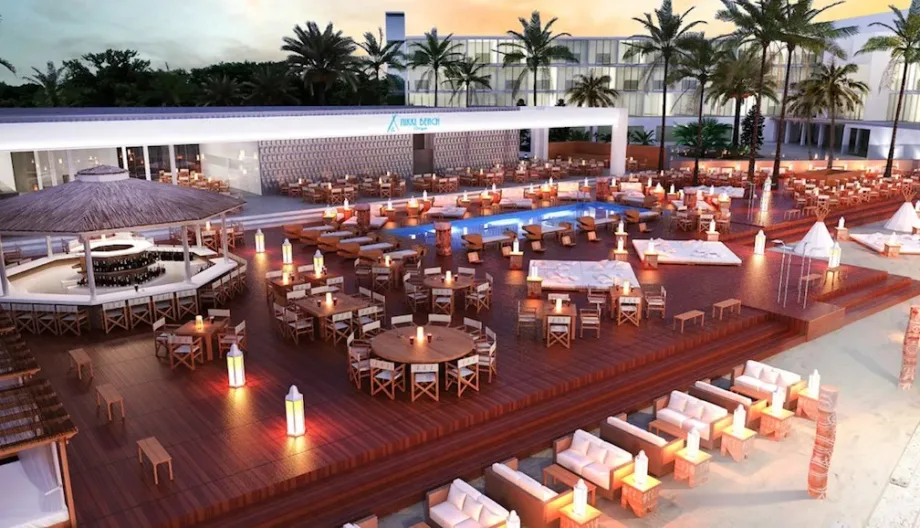 Beachfront resort deck with outdoor dining tables, lounge seating, and a central pool at sunset.