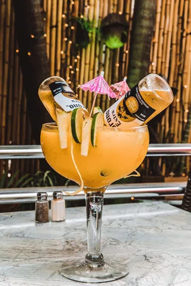 Large tropical cocktail with beer bottles and citrus garnish served at Rakija Lounge Miami Beach