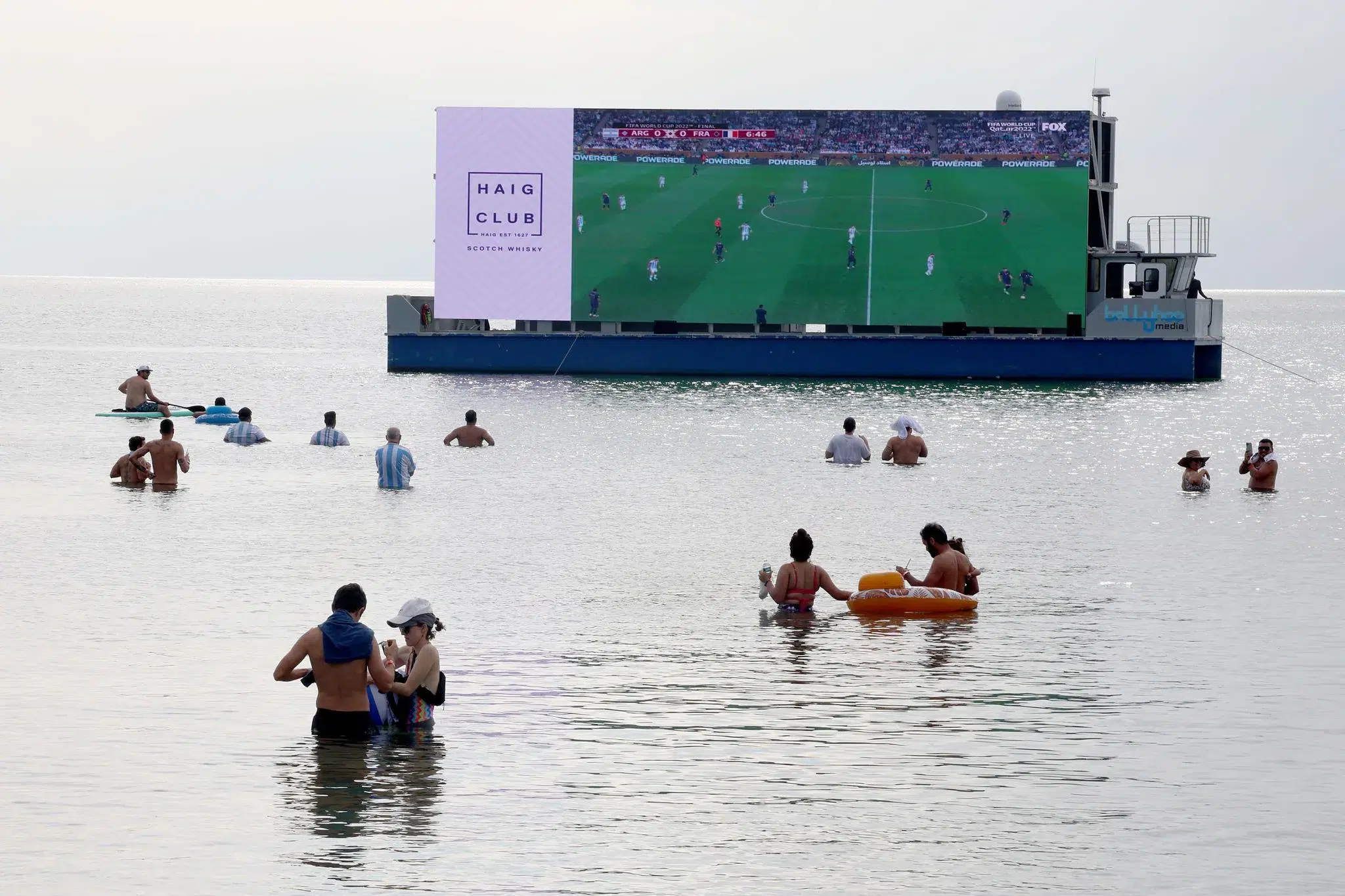 People watching a FIFA World Cup match on a floating giant screen in the ocean during a Miami beach watch party.