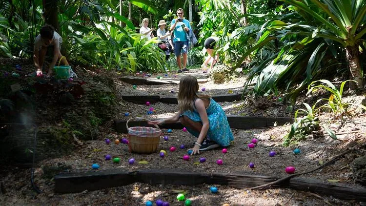 Children collecting colorful Easter eggs during an outdoor Easter egg hunt in a tropical garden park