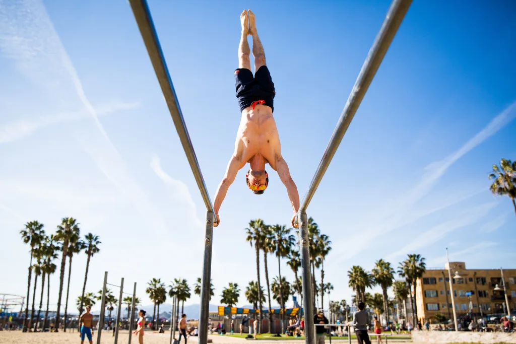 Athlete performing calisthenics workout on bars at Muscle Beach South Beach outdoor gym