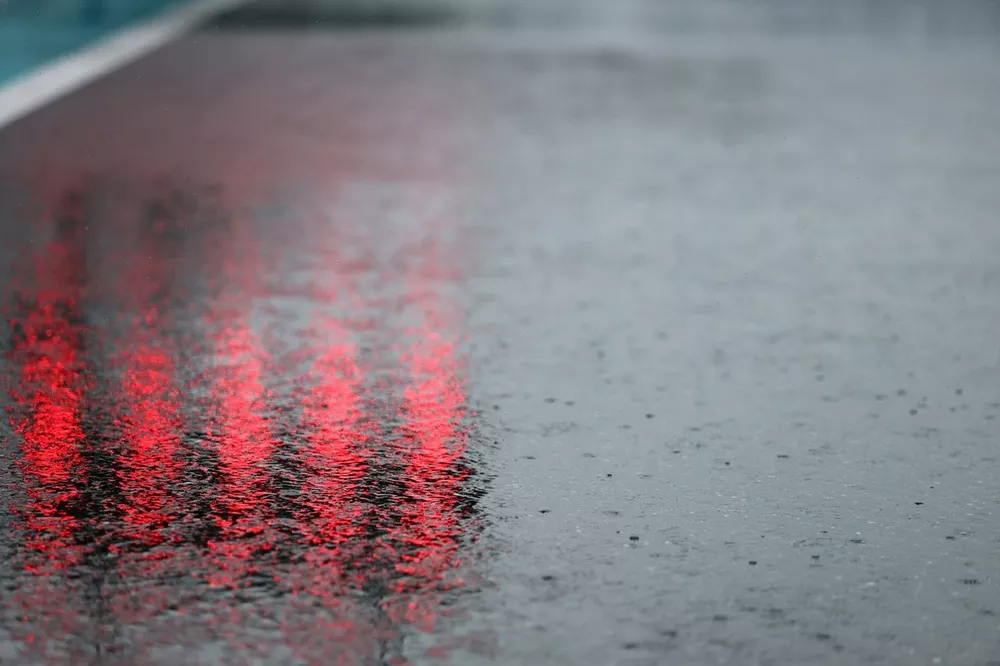 Close-up of wet race track with rain droplets and red light reflections during rainy Formula 1 conditions