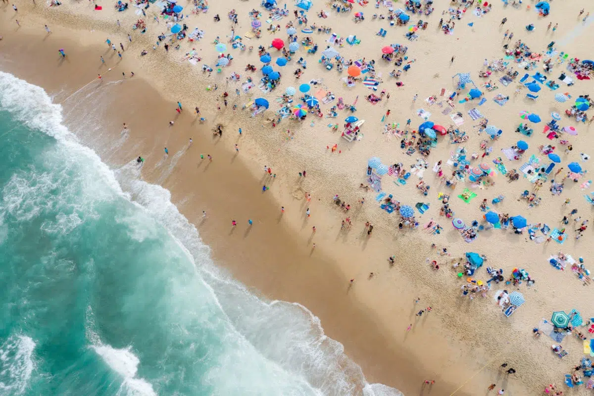 Aerial view of a crowded Miami Beach shoreline filled with umbrellas and visitors enjoying Memorial Day Weekend by the ocean.