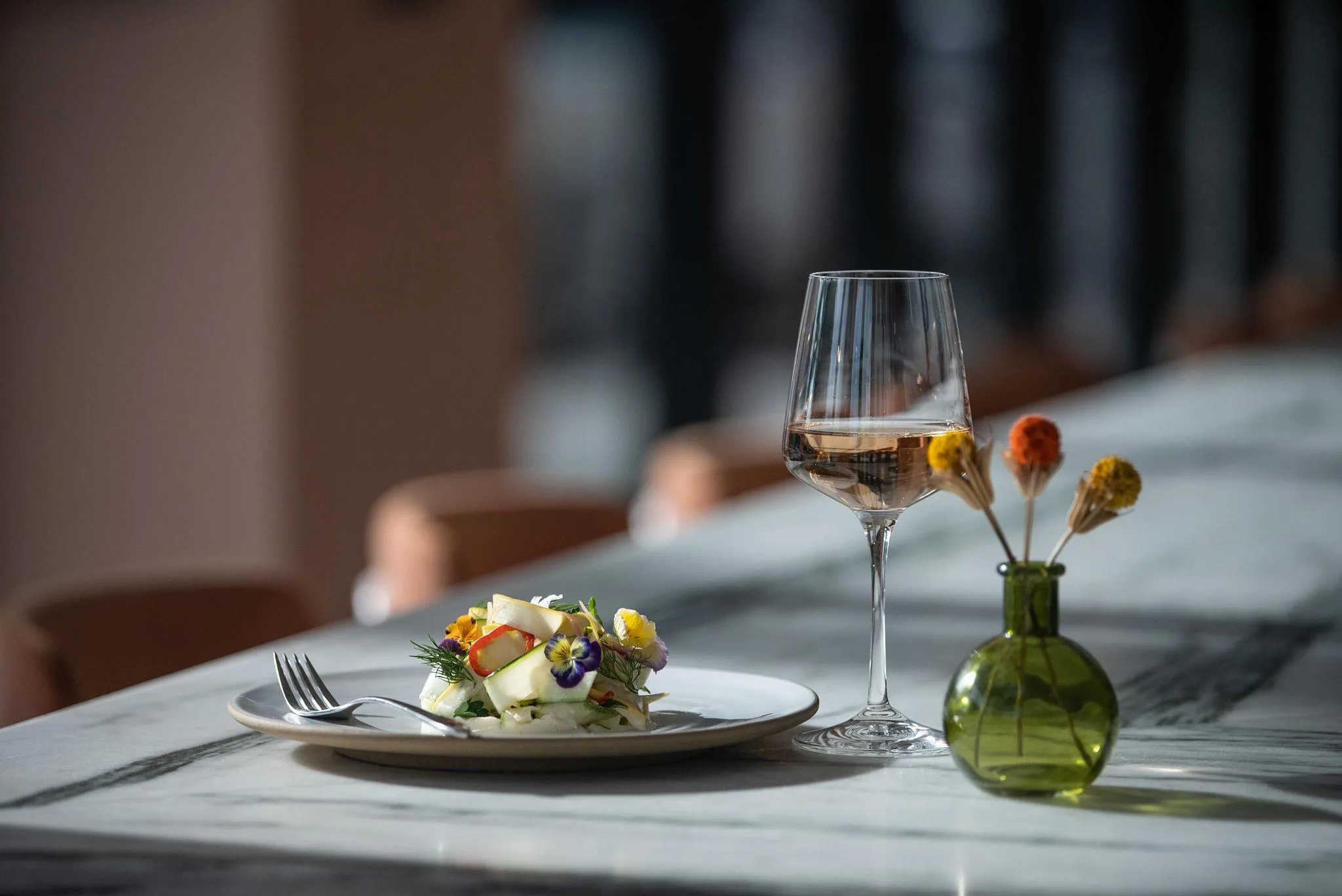 Elegant fine dining setup with plated gourmet dish, wine glass, and floral table decoration in a luxury restaurant