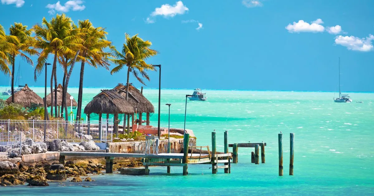 Turquoise waterfront scene in the Florida Keys featuring palm trees, docks, tiki huts, and crystal-clear ocean views during a sunny beach day.