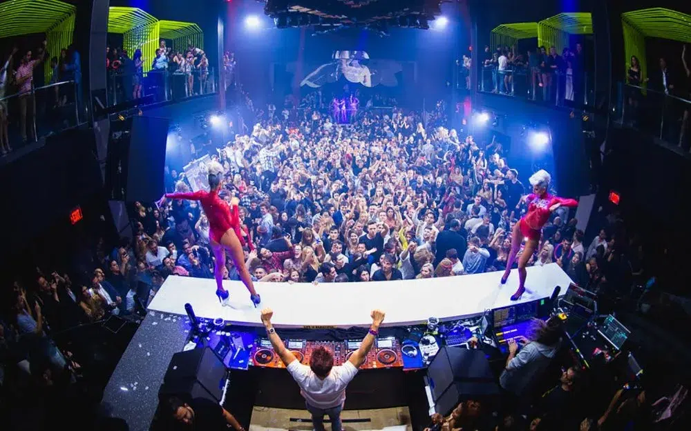 Large crowd inside a Miami nightlife venue watching dancers and DJs perform under colorful lights during an upscale club event.