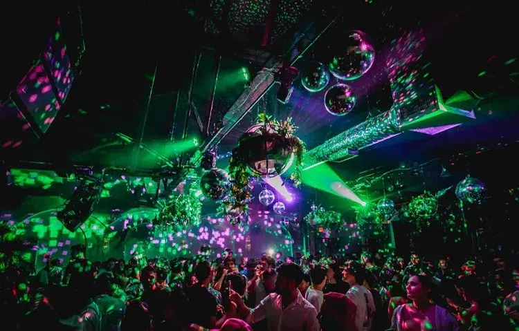 Crowded Miami nightclub with colorful neon lighting, disco balls, and energetic party atmosphere during a late-night entertainment event.