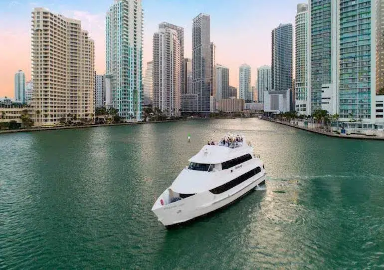 Luxury yacht sailing through Brickell waterfront canals surrounded by Miami high-rise buildings during a sunset boat tour experience.
