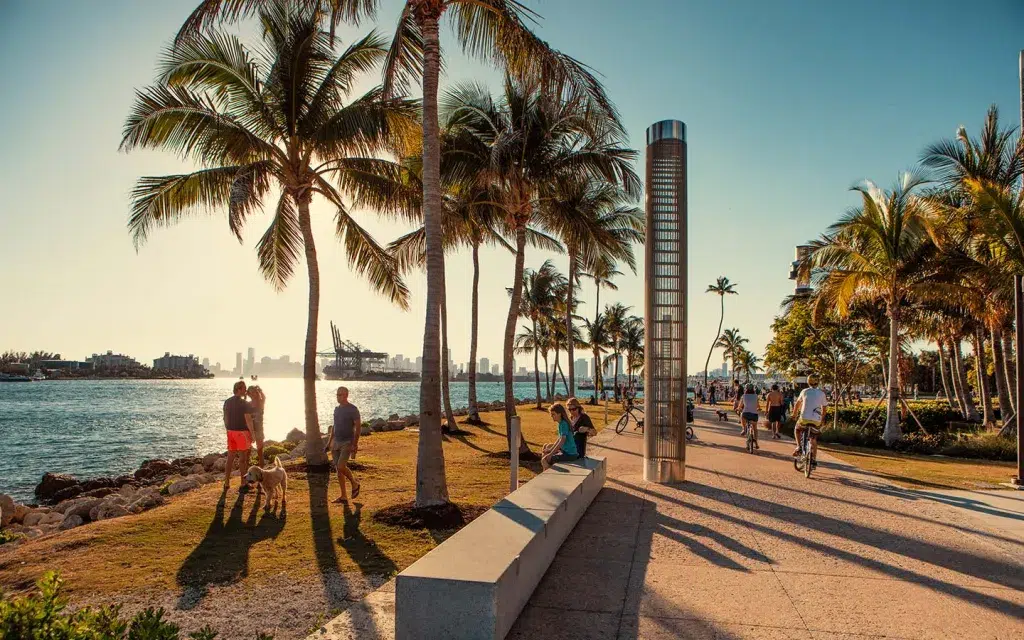 People walking near South Pointe Beach with palm trees, blue sky, and the Atlantic Ocean in the background