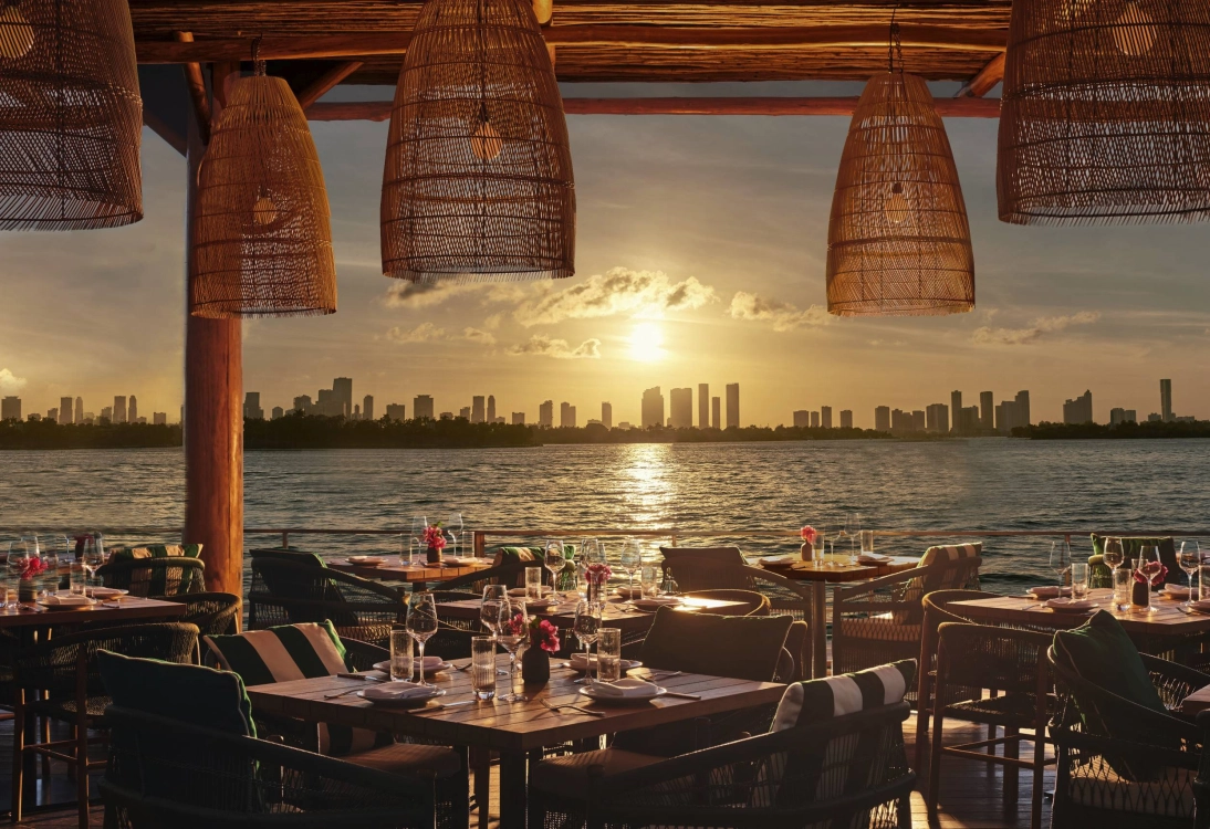 Luxury waterfront dining restaurant in Miami at sunset featuring elegant seating, ocean views, and the Miami skyline in the background.