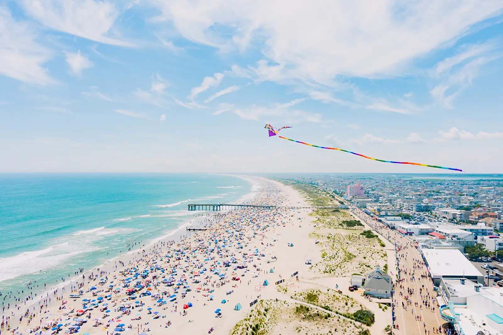 Wide aerial view of Miami Beach packed with beachgoers and colorful kites flying above the coastline during Memorial Day Weekend.
