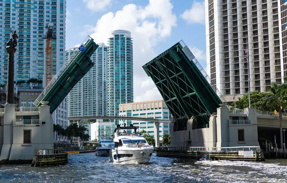 Brickell Avenue Bridge open in Downtown Miami as a yacht passes through the Miami River surrounded by high-rise buildings.