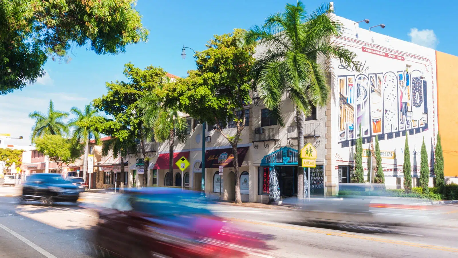 Sunny street view of Little Havana in Miami featuring colorful murals, palm trees, and local shops along Calle Ocho.