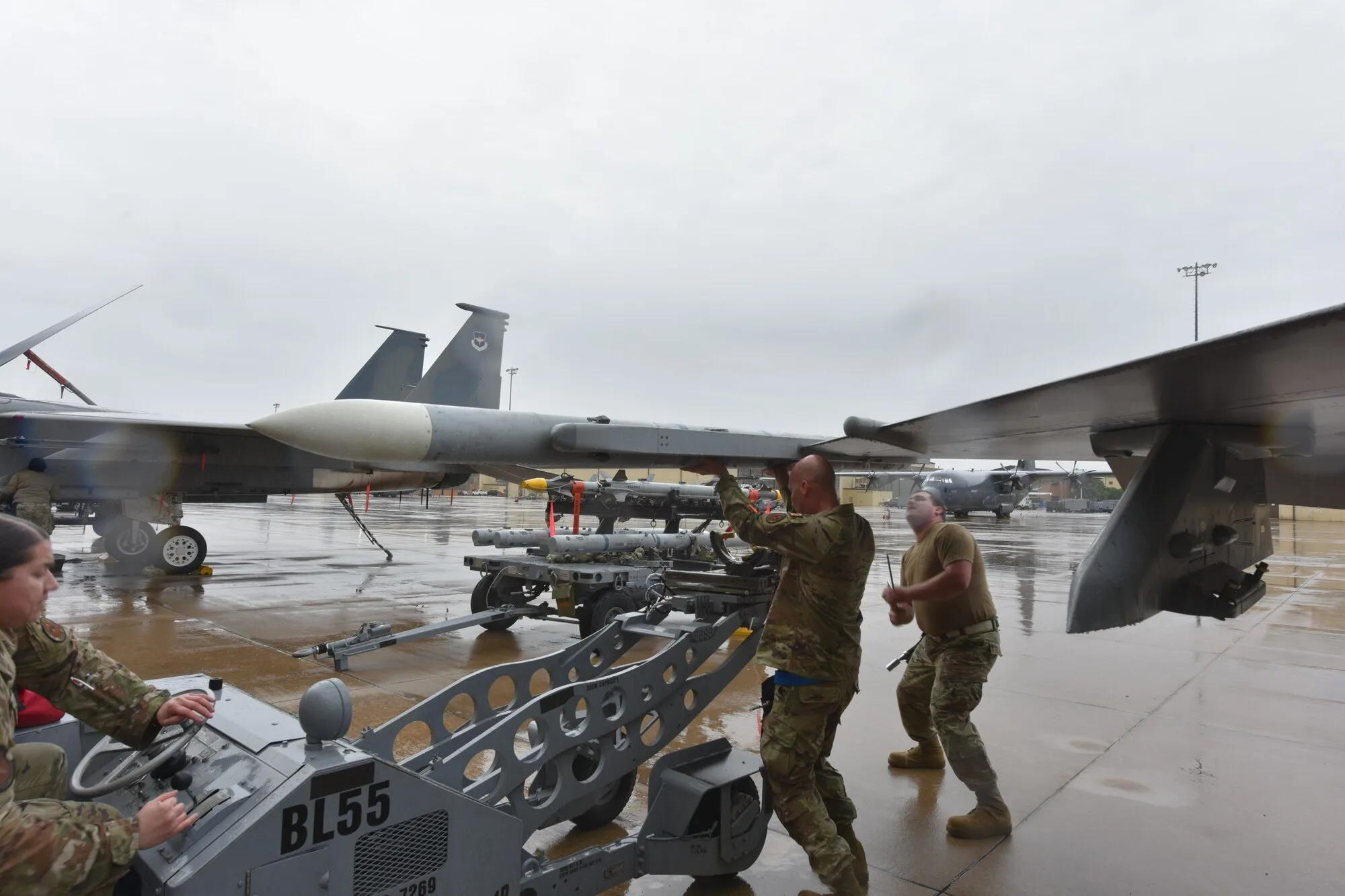 Military personnel working beside a fighter jet on a rainy airfield during a military aviation demonstration ahead of Memorial Day Weekend events.