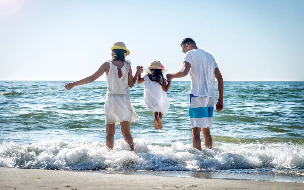 Family walking along the shoreline and playing in ocean waves on a sunny Miami beach during Memorial Day Weekend.