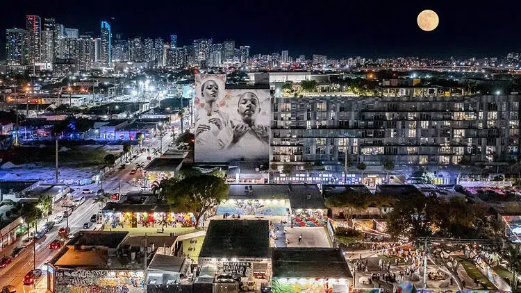 Aerial nighttime view of Wynwood Miami filled with restaurants, bars, murals, crowds, and city lights, showcasing the neighborhood’s vibrant nightlife and entertainment atmosphere.