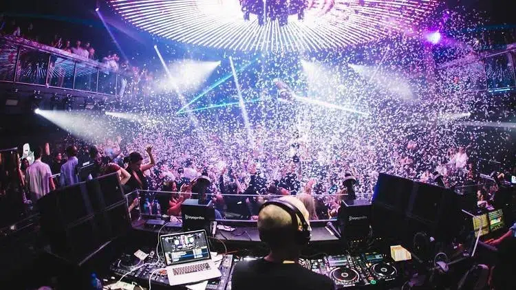 Packed Miami nightclub with a live DJ performance, confetti effects, bright stage lighting, and a high-energy crowd celebrating during a late-night party event.
