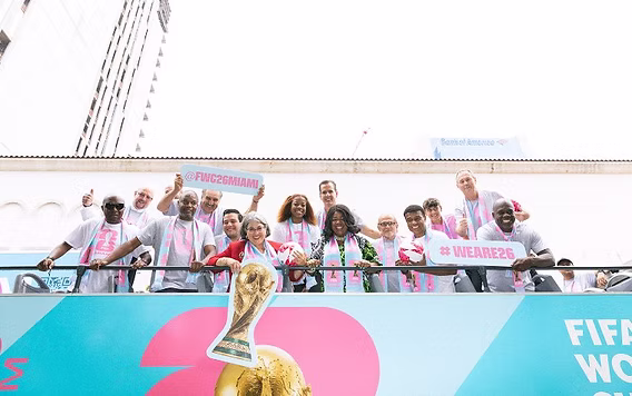 Group of fans celebrating at a FIFA World Cup Miami 2026 promotional event with the World Cup trophy displayed in front of a branded viewing platform.