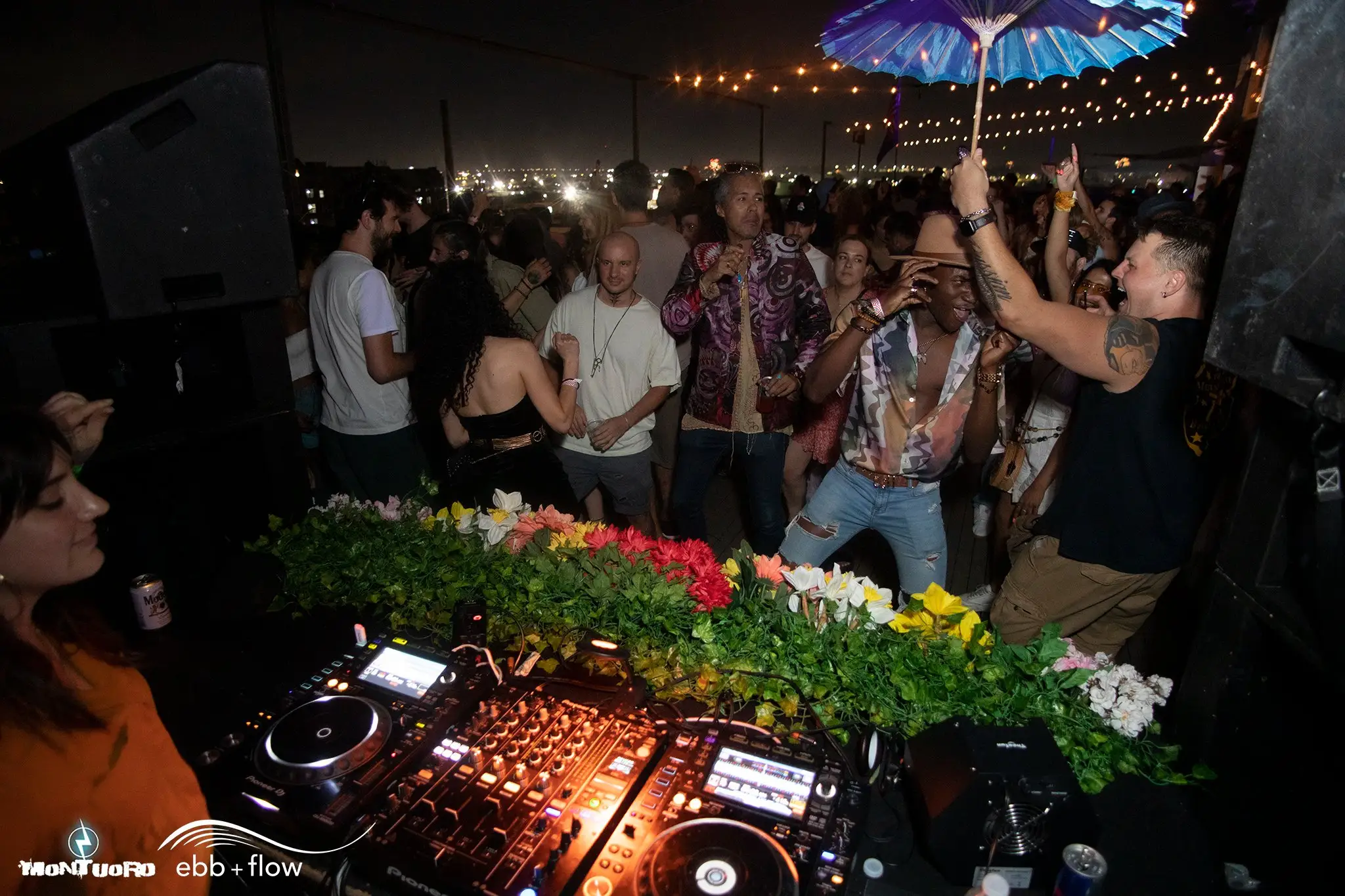 DJ performing at a packed rooftop party in Miami with guests dancing under string lights and enjoying Fourth of July weekend nightlife overlooking the city skyline.
