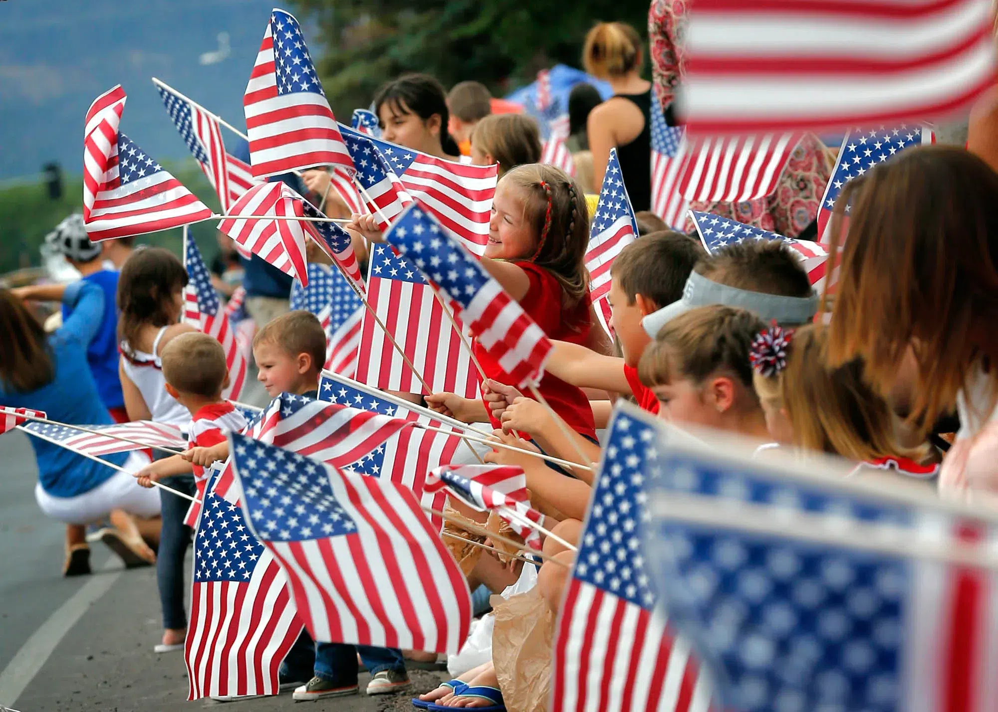 Families and children waving American flags during a Fourth of July parade, celebrating Independence Day with patriotic community events and festive gatherings.