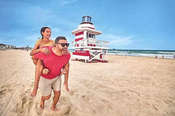 Father carrying his daughter on his shoulders near a South Beach lifeguard tower, enjoying a fun-filled Father's Day weekend on Miami Beach.