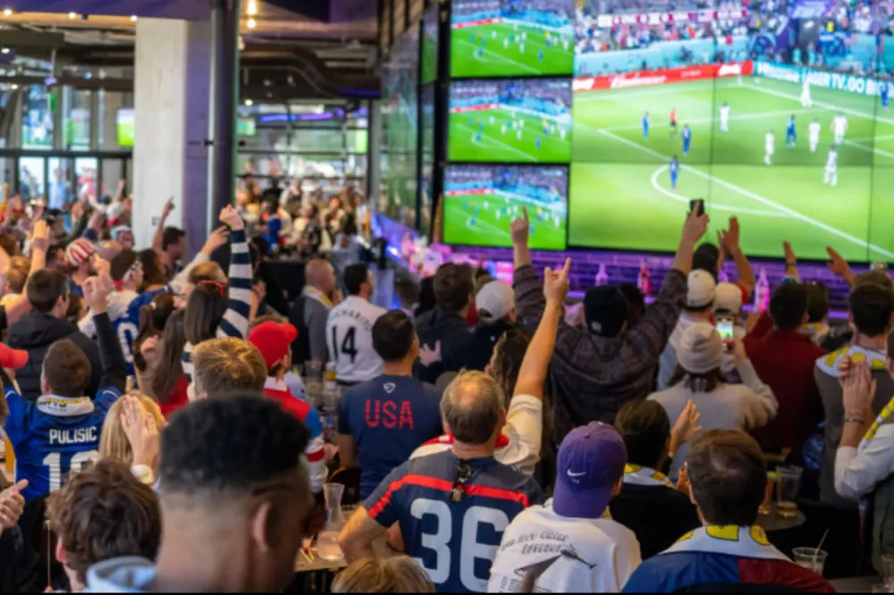Crowd of soccer fans cheering inside a sports bar while watching a FIFA World Cup match on large screens during a lively watch party event.
