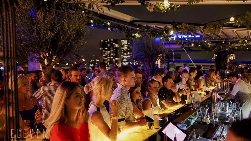 Crowded rooftop bar in Miami featuring cocktails, city views, and a lively social atmosphere during a summer nightlife event and Fourth of July celebration.