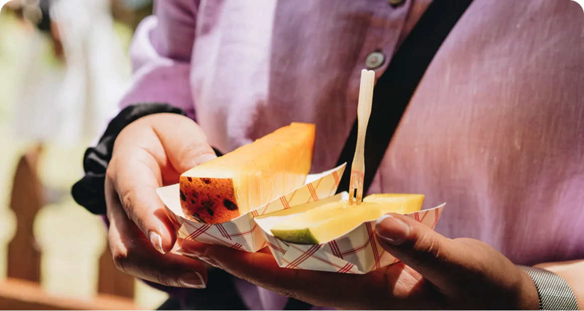 Visitor holding samples of fresh mango slices during a tasting experience at the Miami Mango Festival, showcasing unique tropical fruit varieties from South Florida and beyond.