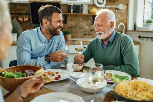 Father and adult son sharing a meal and conversation at a family dinner table, celebrating Father's Day with food, drinks, and quality time together.