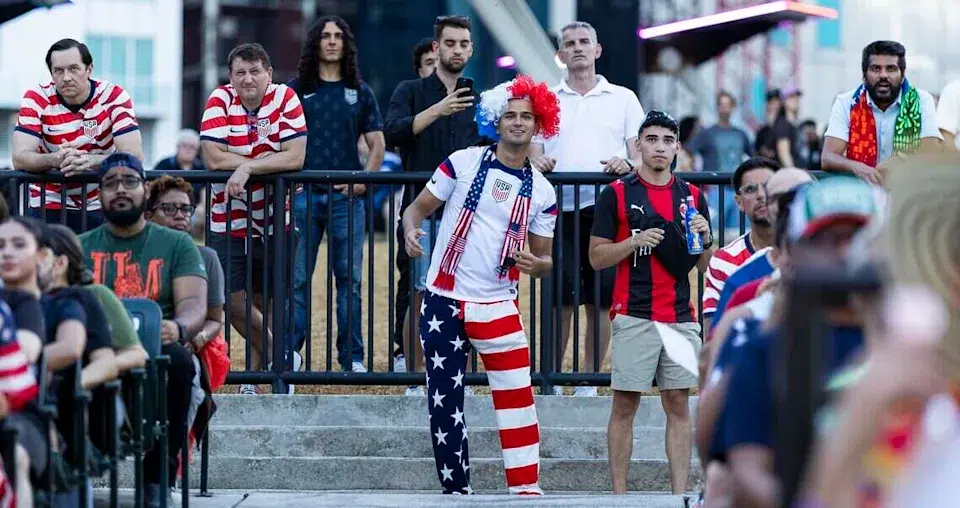 Soccer fans wearing patriotic red, white, and blue outfits gather outside a Miami stadium before a match, creating a lively game-day atmosphere.