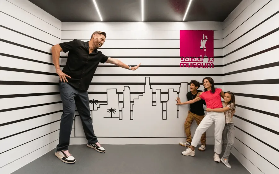 Family enjoying an interactive optical illusion exhibit at Paradox Museum Miami, where perspective creates the appearance of a giant figure inside a distorted room.