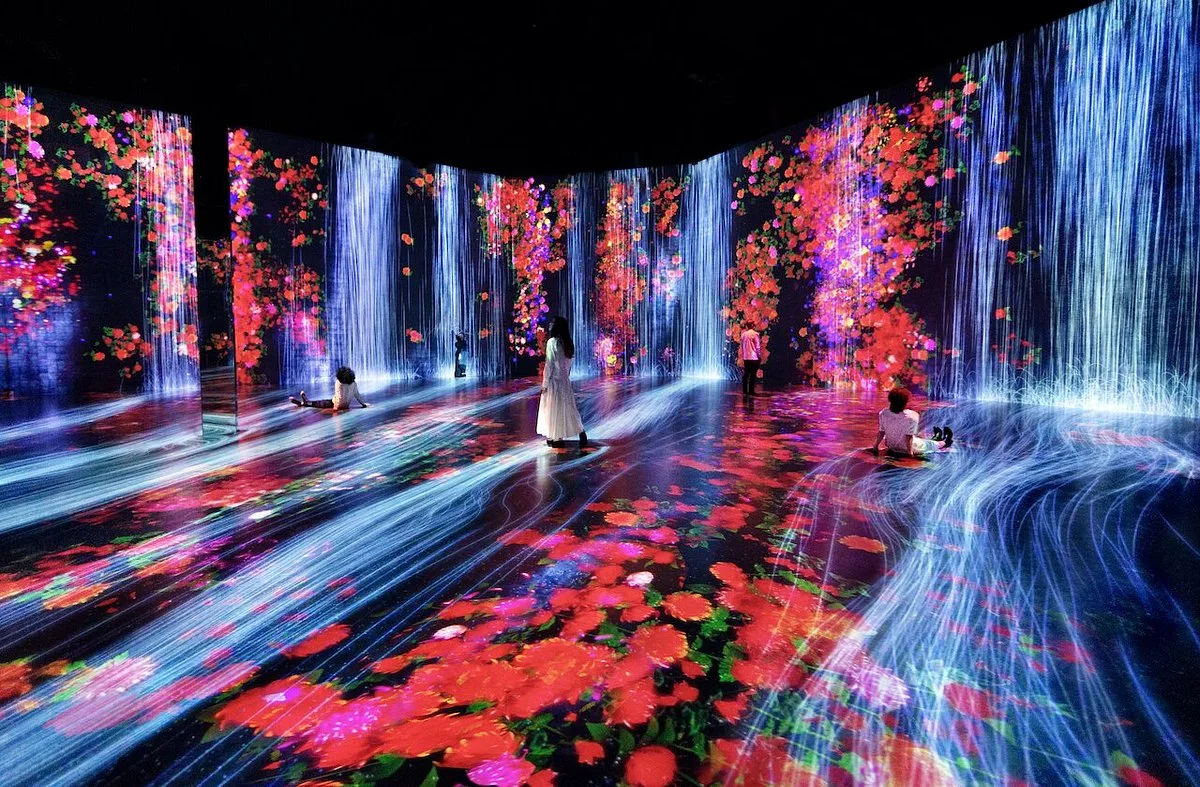 Guests exploring a vibrant immersive digital art exhibition at Superblue Miami, featuring colorful animated floral projections and floor-to-ceiling interactive light displays.